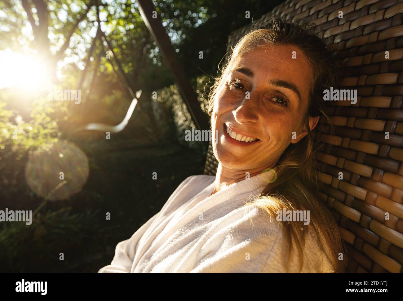 Frau lächelt auf einer Gartenschaukel, die Sonne scheint durch die Bäume Stockfoto