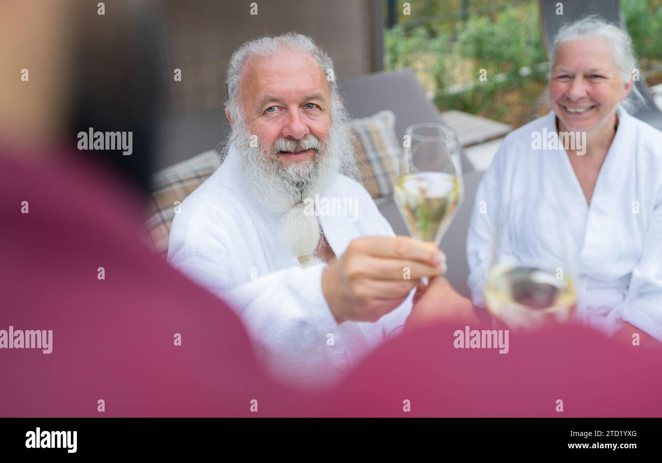 Seniorenpaar in weißen Bademänteln, die Champagner von einem Kellner in einem Wellnesshotel erhalten. Bild des Konzepts zum Geburtstag und Valentinstag Stockfoto