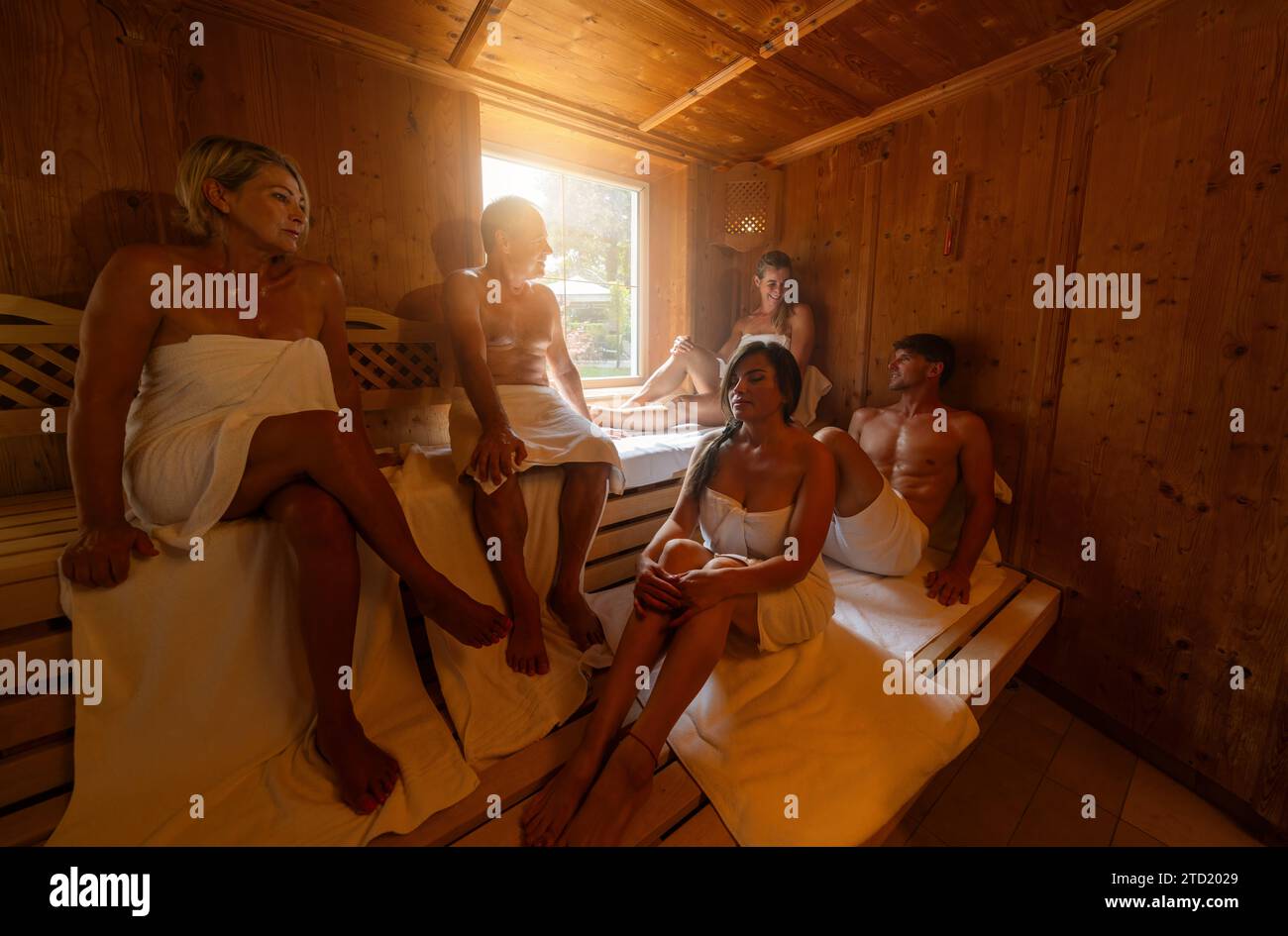 Die Leute sitzen in der Sauna, einige reden und entspannen sich zusammen in der heißen finnischen Sauna. Dramatisches Licht mit Dampfbad, Spa und Wellness-Konzept. Stockfoto