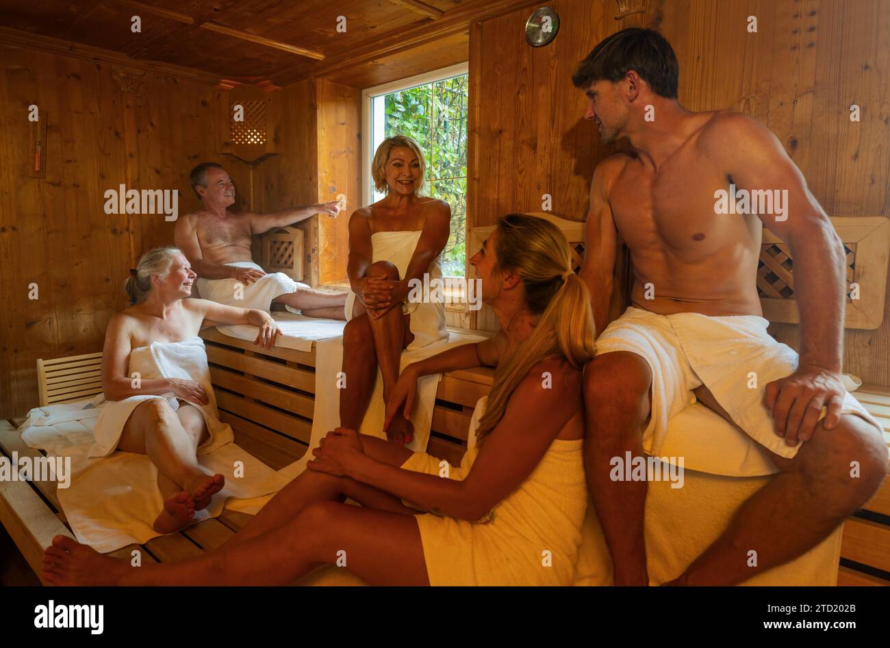 Menschen jeden Alters entspannen gemeinsam in der heißen finnischen Sauna. Dramatisches Licht mit Dampfbad, Spa und Wellness-Konzept. Stockfoto