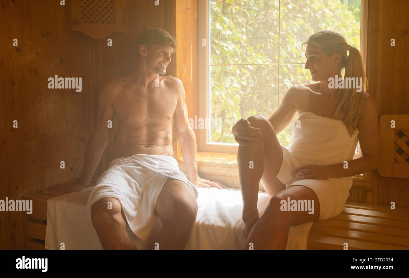 Mann und Frau sitzen in der finnischen Sauna und lächeln einander an, in Handtücher gewickelt. Spa Wellness Hotel Konzept Bild Stockfoto