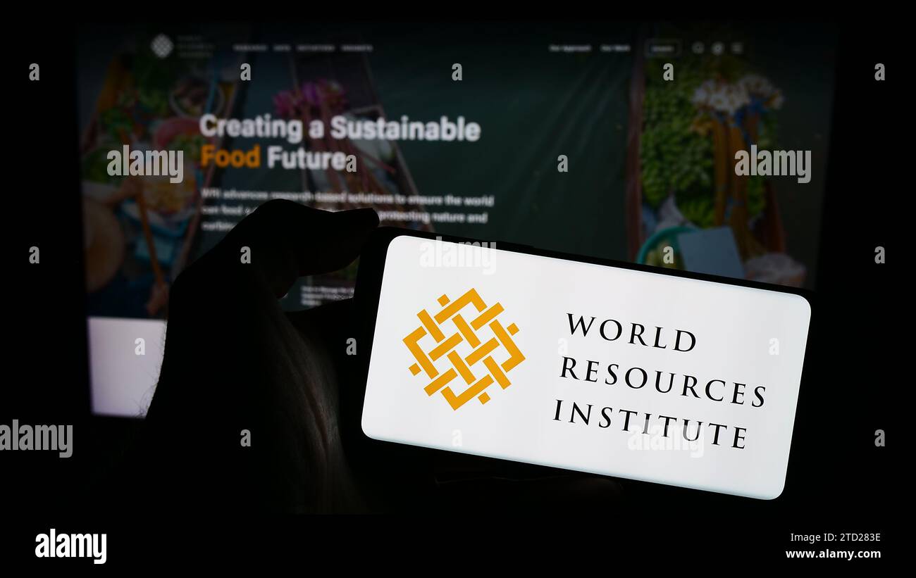 Person, die ein Mobiltelefon mit dem Logo der Forschungsorganisation World Resources Institute (WRI) vor der Webseite hält. Schwerpunkt auf dem Display des Telefons. Stockfoto