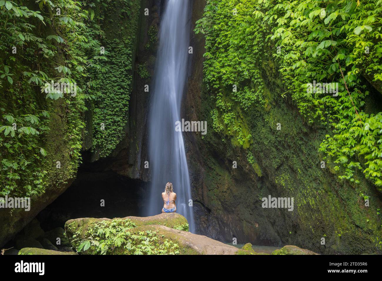 Eine junge Frau im Badeanzug am Wasserfall Leke Leke im üppigen tropischen Wald, Bali, Indonesien Stockfoto