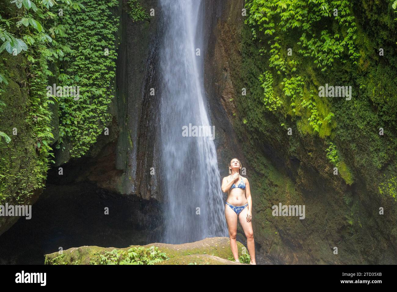 Eine junge Frau im Badeanzug am Wasserfall Leke Leke im üppigen tropischen Wald, Bali, Indonesien Stockfoto