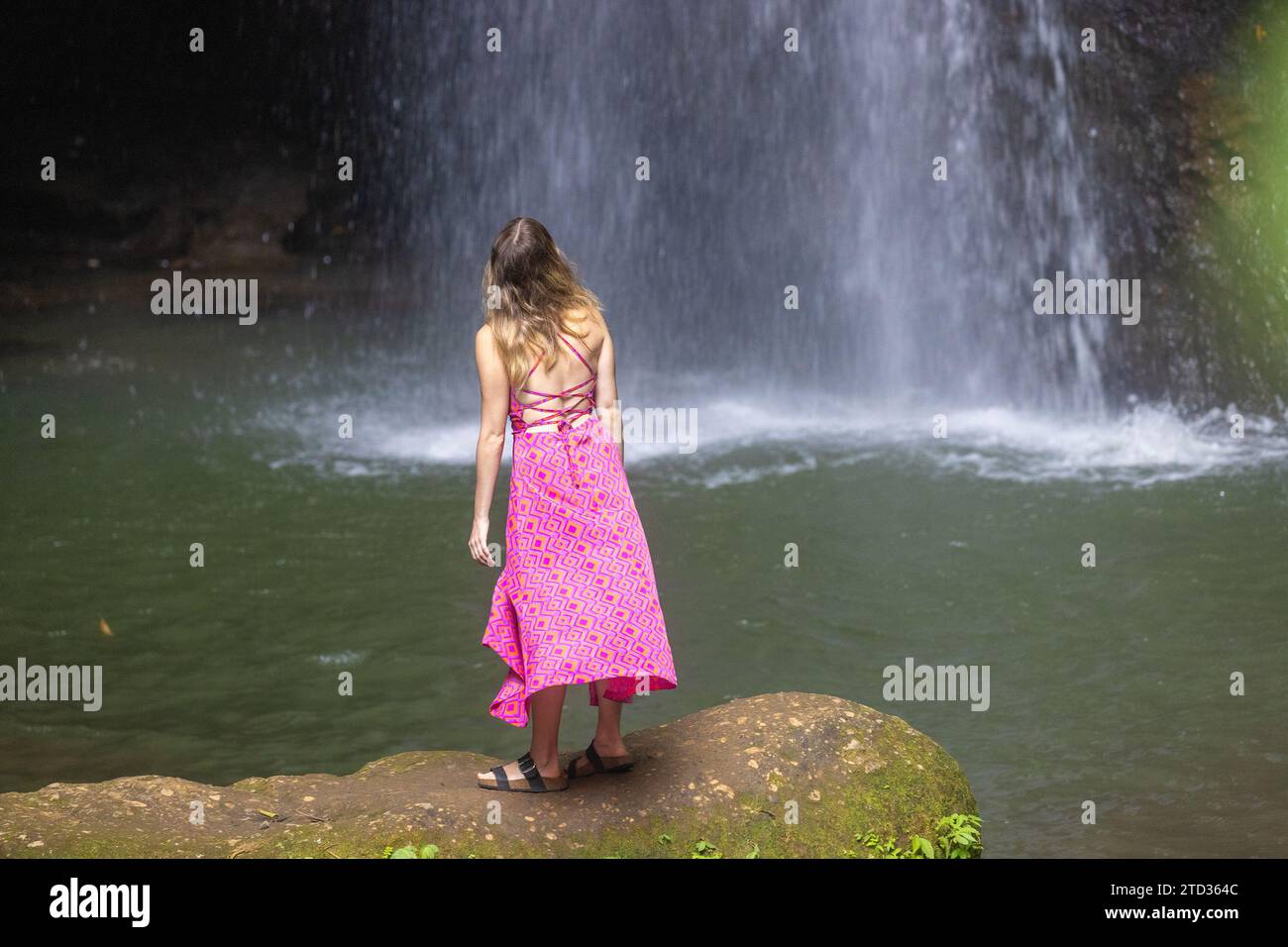 Eine junge Frau in einem rosa Kleid am Wasserfall Leke Leke in einem üppigen tropischen Wald, Bali, Indonesien Stockfoto