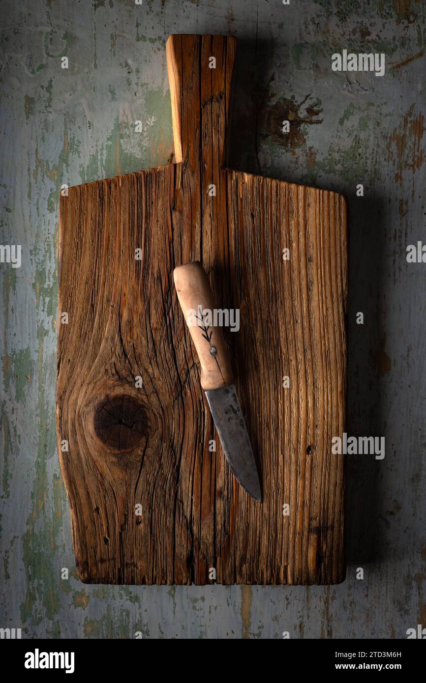 Kleines Messer mit Holzgriff, das auf einem alten Schneidebrett auf einem rostigen alten Tisch liegt Stockfoto