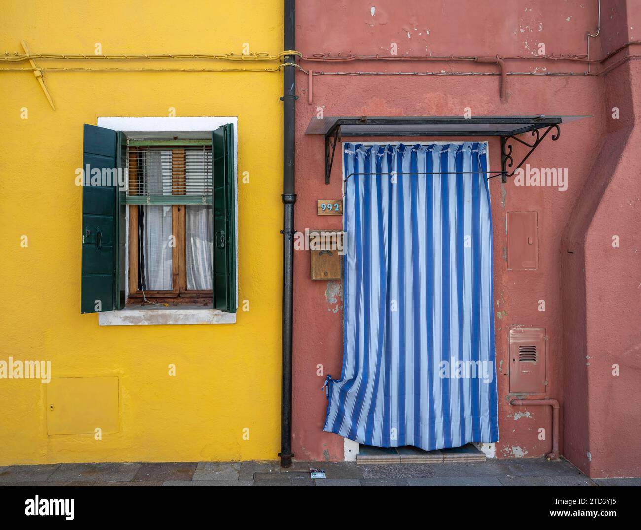 Rot-gelbe Hausfassade mit Eingangstür mit blau-weißen Vorhängen und Fenstern, farbenfrohe Häuser auf der Insel Burano, Venedig, Venetien Stockfoto