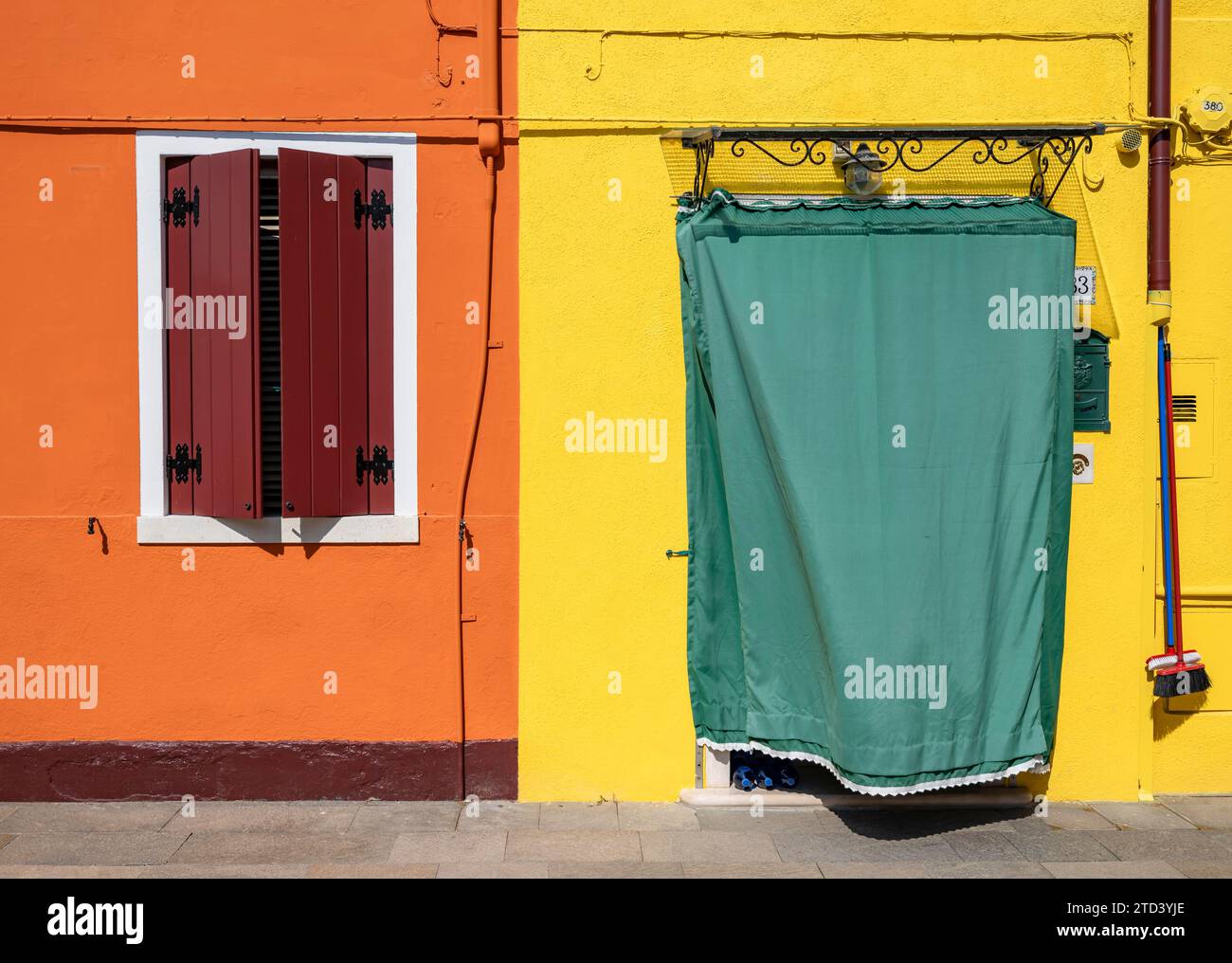 Orange und gelbe Hausfassade mit Eingangstür mit grünen Vorhangfenstern, farbenfrohe Häuser auf der Insel Burano, Venedig, Venetien, Italien Stockfoto