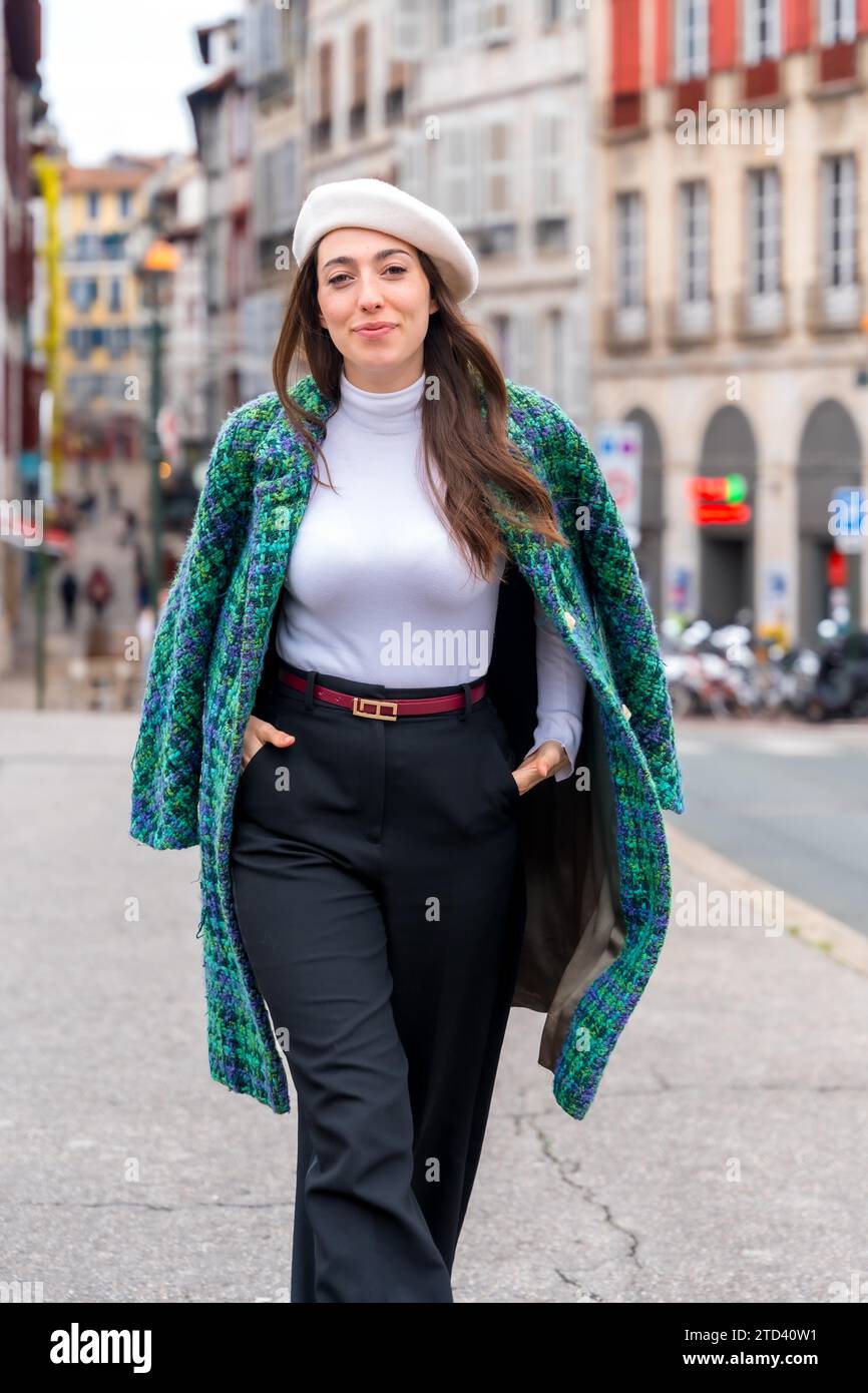 Vertikales Foto einer modischen Frau, die lächelt, während sie eine schöne Stadt erkunden Stockfoto