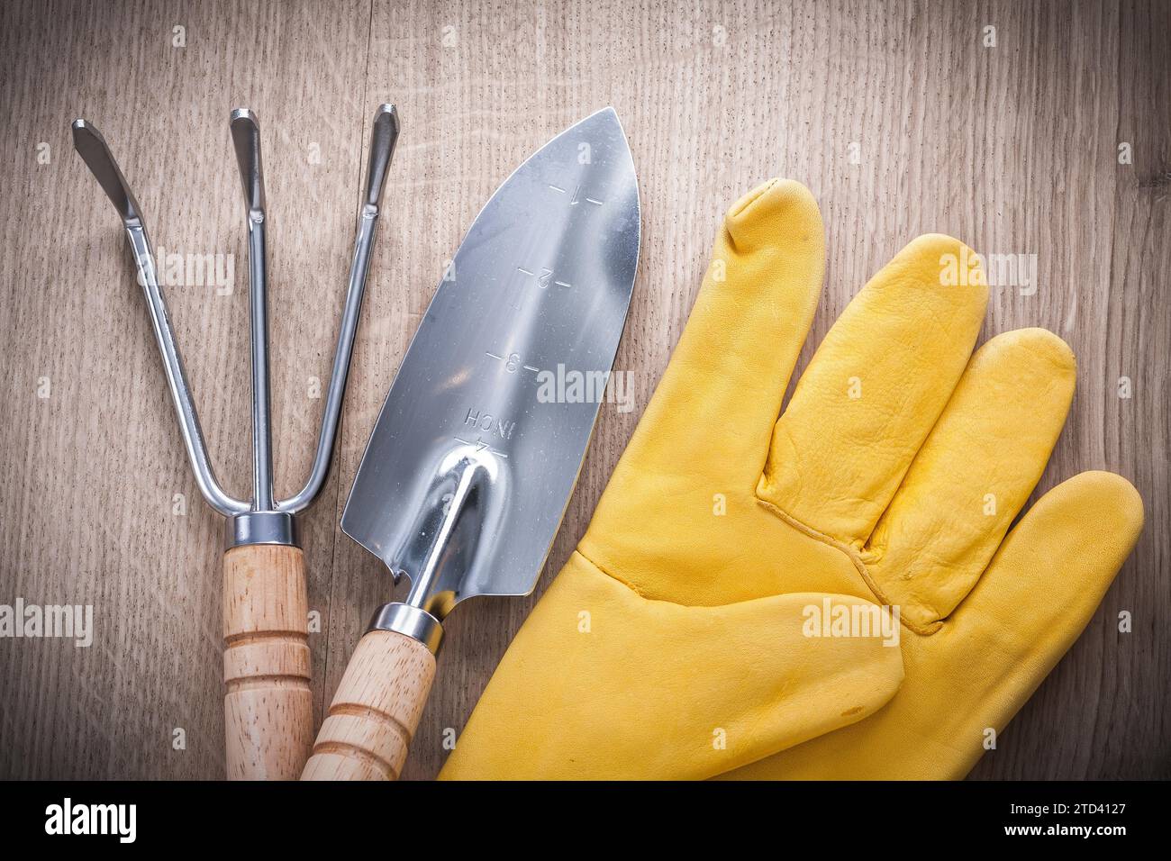 Nahaufnahme einer Gartenkelle aus Stahl mit Handspaten und Ledersicherheitshandschuhen auf Holzbrett Landwirtschaftskonzept Stockfoto