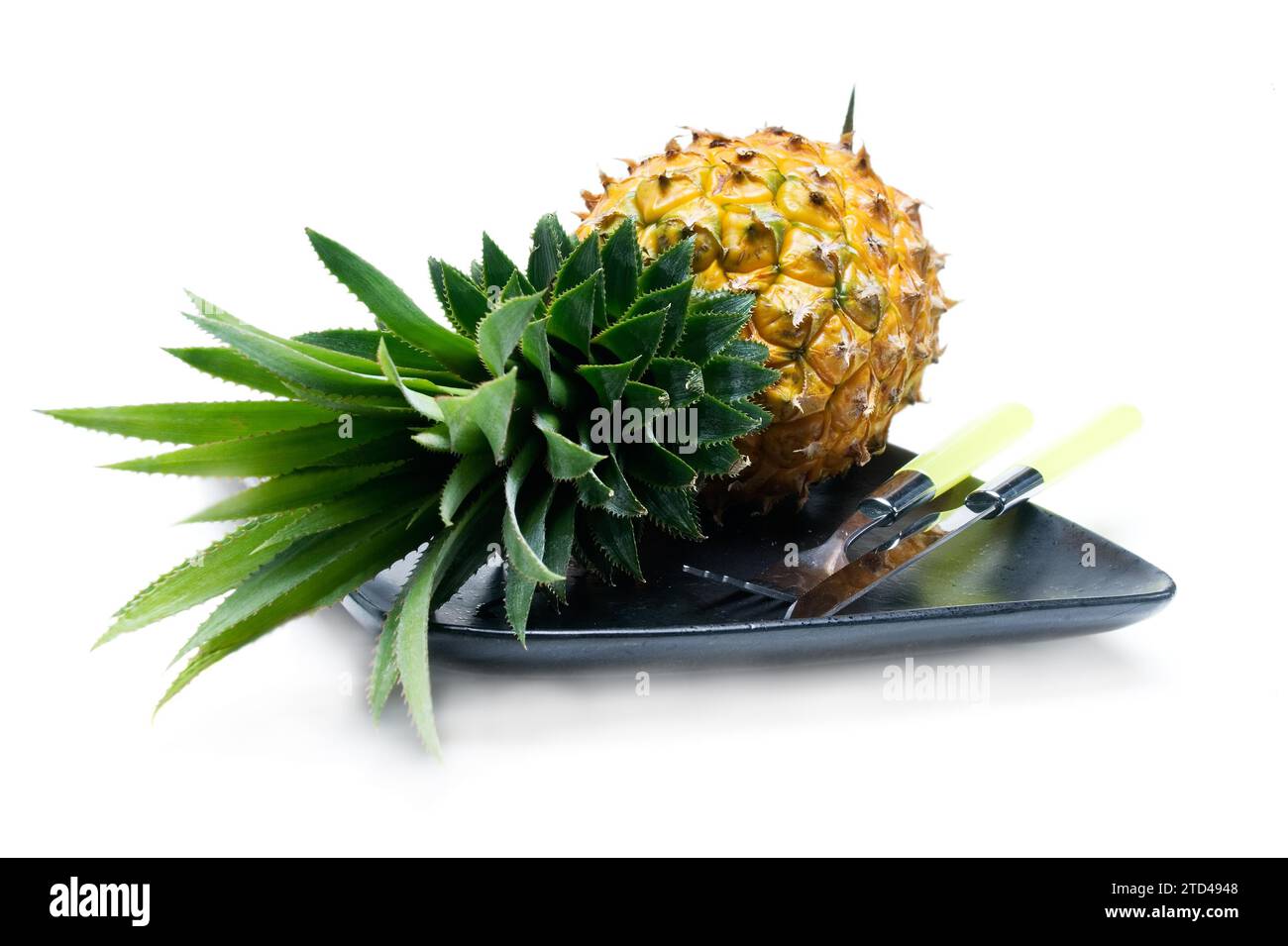 Ananas auf einem schwarzen Teller mit Messer und Gabel isoliert auf weißem Hintergrund, Lebensmittelfotografie Stockfoto