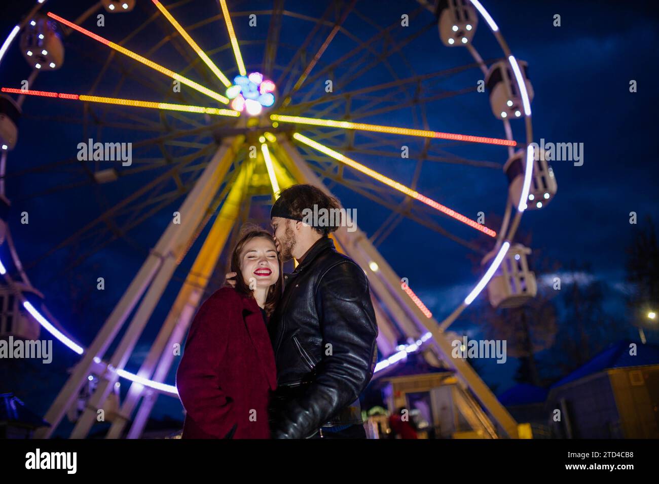 Verliebtes Paar in einem Vergnügungspark in der Nähe eines Riesenrads bei einem Date bei kaltem Wetter. Das Konzept von Liebe und Freude in Beziehungen Stockfoto