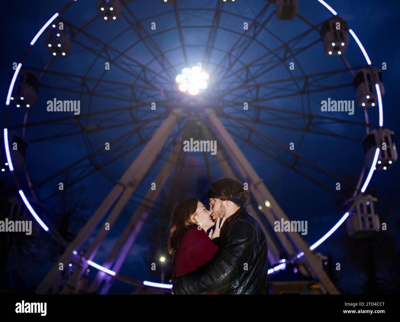 Verliebtes Paar in einem Vergnügungspark in der Nähe eines Riesenrads bei einem Date bei kaltem Wetter. Das Konzept von Liebe und Freude in Beziehungen Stockfoto