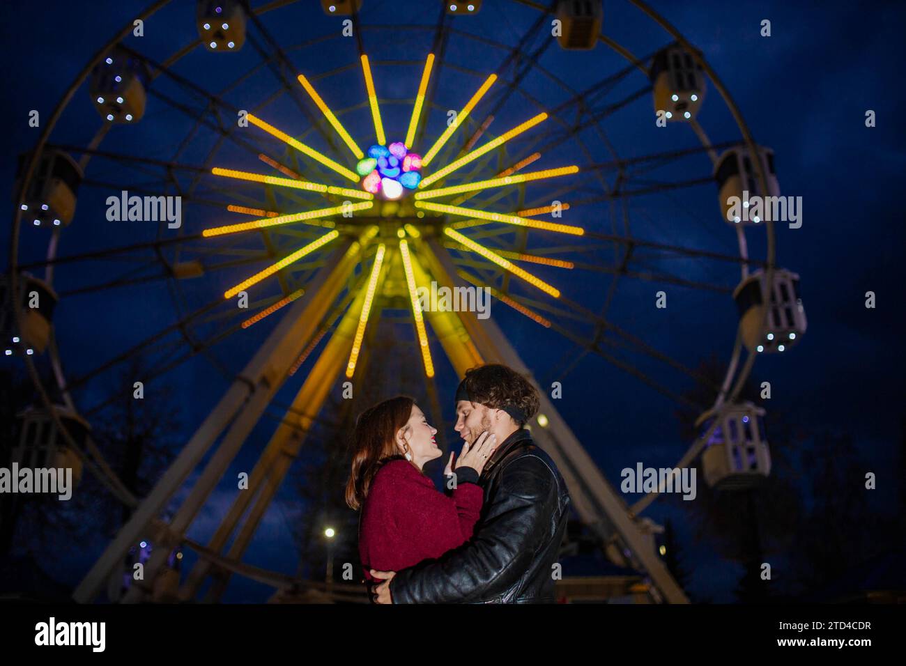Verliebtes Paar in einem Vergnügungspark in der Nähe eines Riesenrads bei einem Date bei kaltem Wetter. Das Konzept von Liebe und Freude in Beziehungen Stockfoto