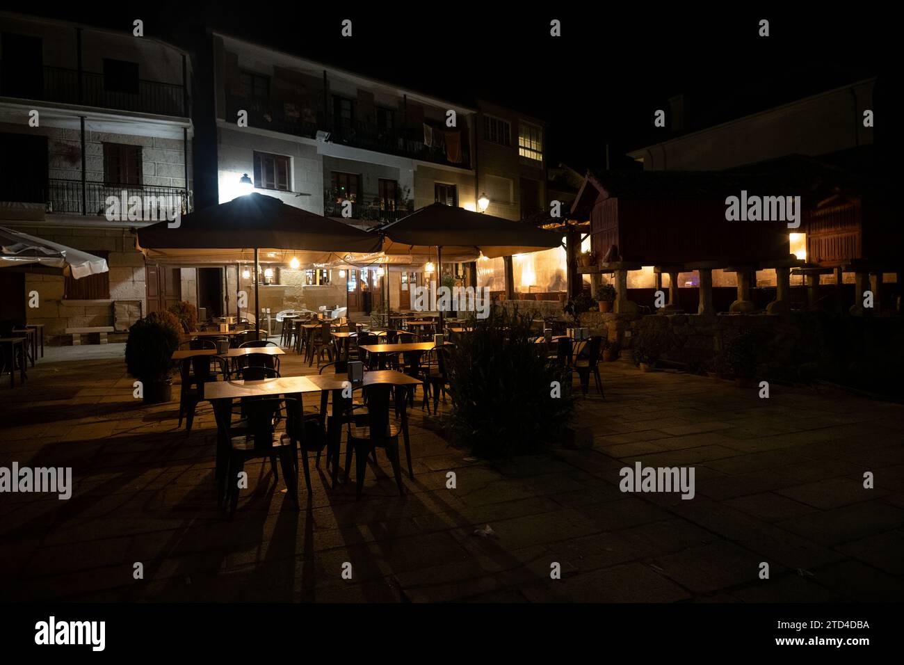 Gemütliches Restaurant im Freien bei Nacht mit beleuchteten Sonnenschirmen und leeren Tischen, einladendes Ambiente in ruhiger urbaner Umgebung. Stockfoto