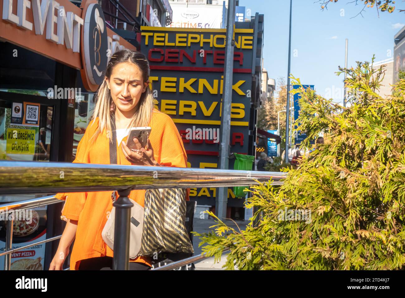Die junge türkische Frau läuft, während sie ihr Smartphone in der Nähe des teknik Servis Ladenschilds ansieht. Ankara Türkei Stockfoto