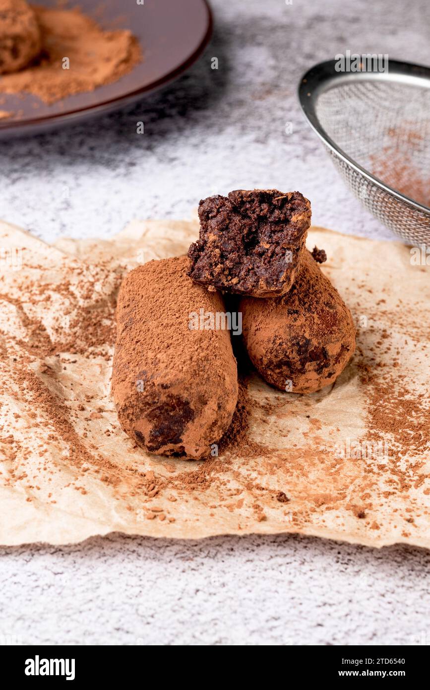 Schokoladen-Kartoffelkuchen. Keks mit Sahne und Kakaopulver auf Teller. Trüffeldessert, bestreut mit Kakaopulver und Tasse Tee auf weißem Tisch. Stockfoto