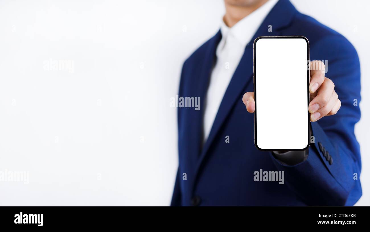 Geschäftsmann Hand hält mobiles weißes leeres Display, Mock Up Handy Handy im Anzug hält Handy mit leerem weißen Bildschirm auf dunkelblauem B Stockfoto