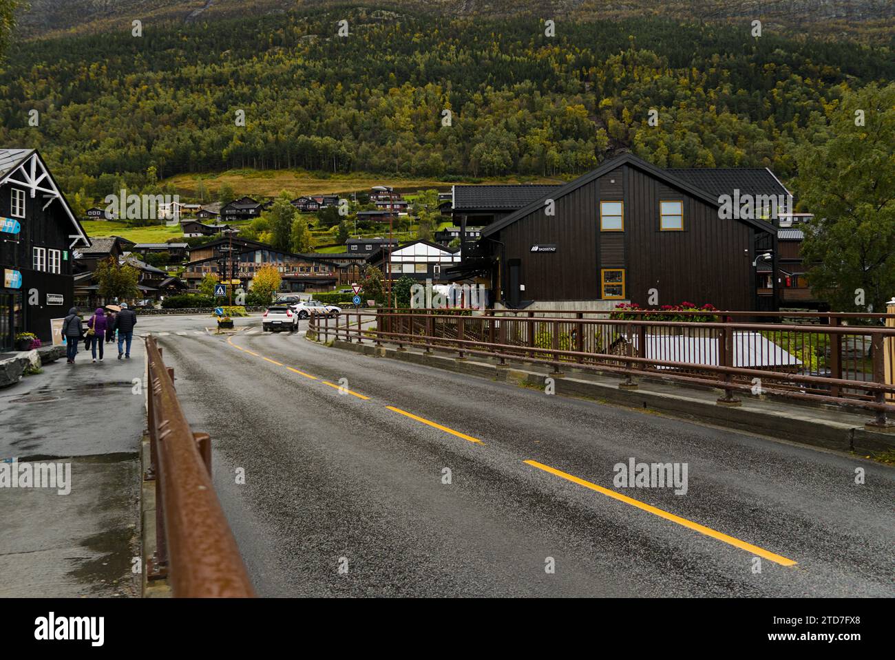 Die asphaltierte Straße führt an einer kleinen Stadt mit Bergen im Hintergrund vorbei. Stockfoto
