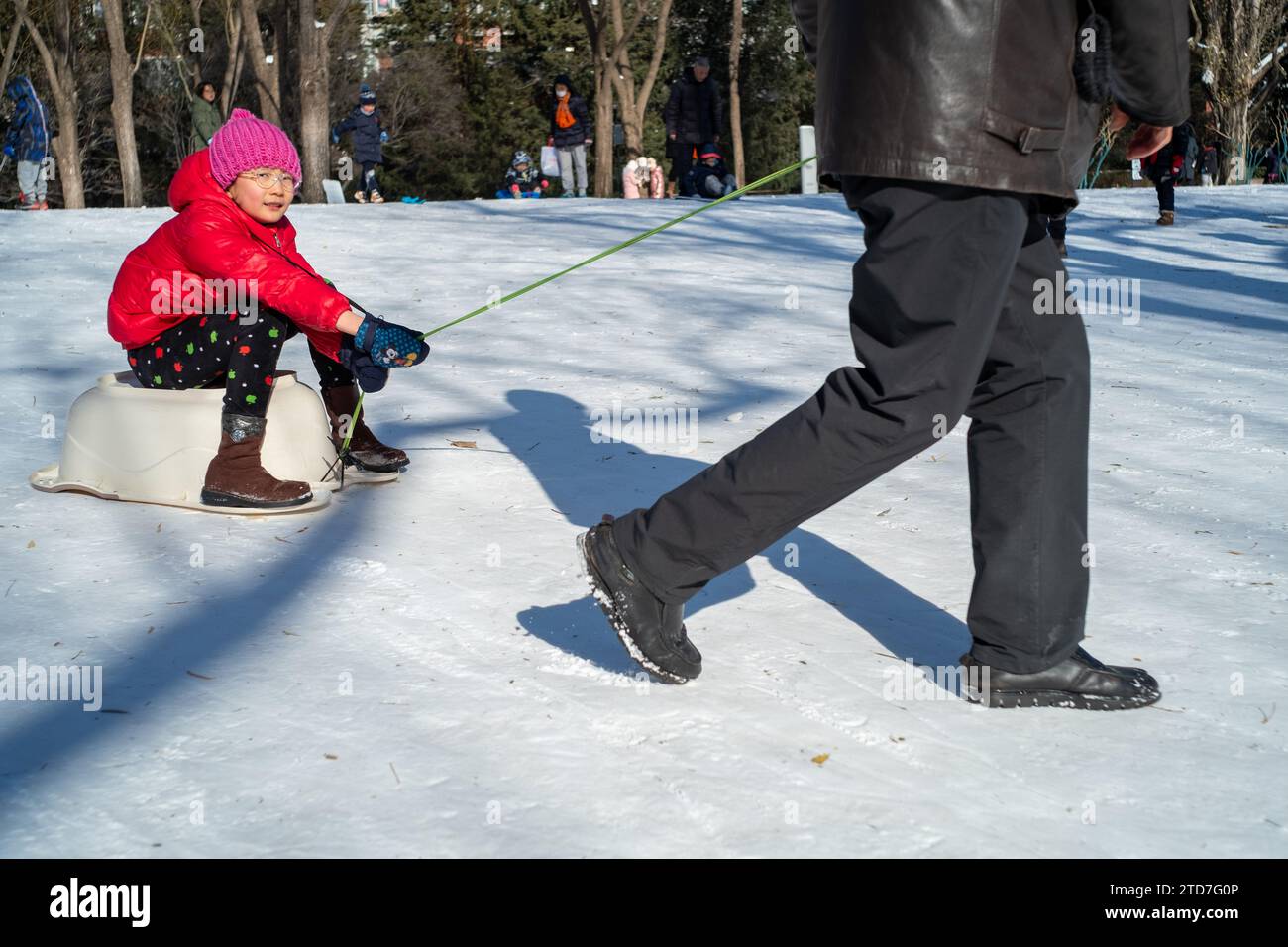 Ein chinesisches Mädchen und ihr Großvater spielen im Schnee in einem Park in Peking, China.17 Dez-2023 Stockfoto