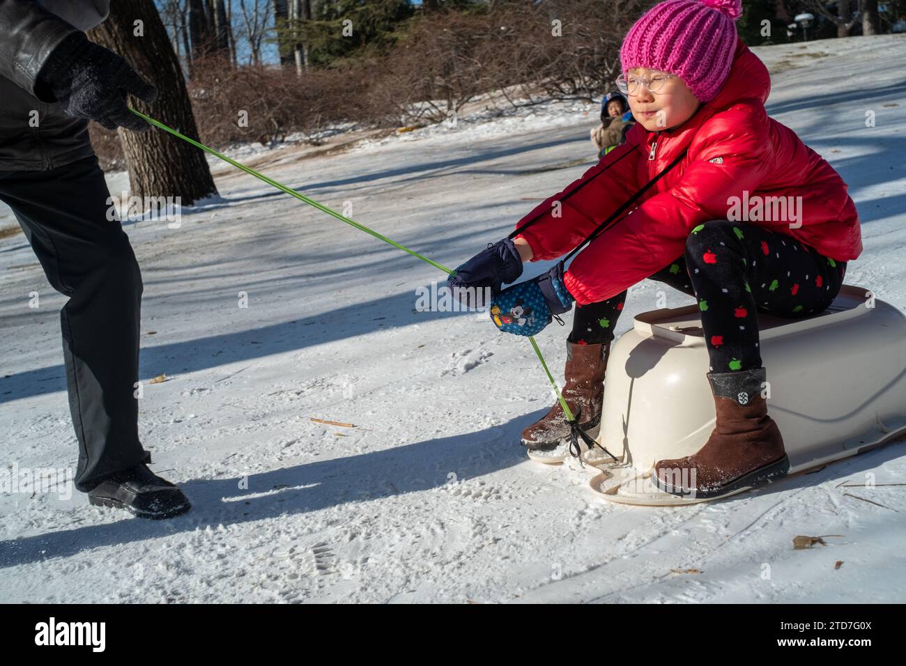 Ein chinesisches Mädchen und ihr Großvater spielen im Schnee in einem Park in Peking, China.17 Dez-2023 Stockfoto