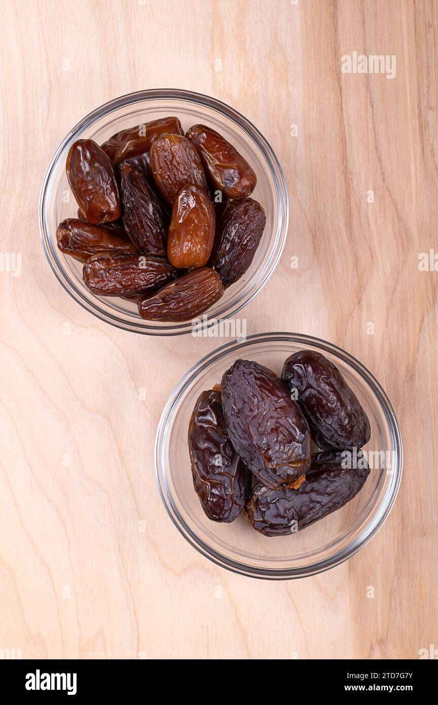 Deglet Nour und Medjool Datteln, in Glasschalen, auf Holztafel, von oben. Sonnengetrocknete und süße Dattelsorten. Stockfoto