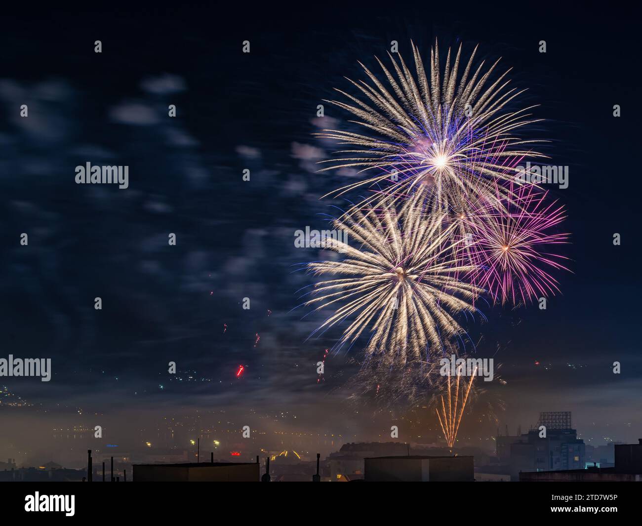 Buntes, helles Feuerwerk am Nachthimmel. Kleine Stadt feiert Feiertage mit festlichen Feuerwerksexplosionen. Langbelichtungsaufnahme. Städtische Nacht. Stockfoto
