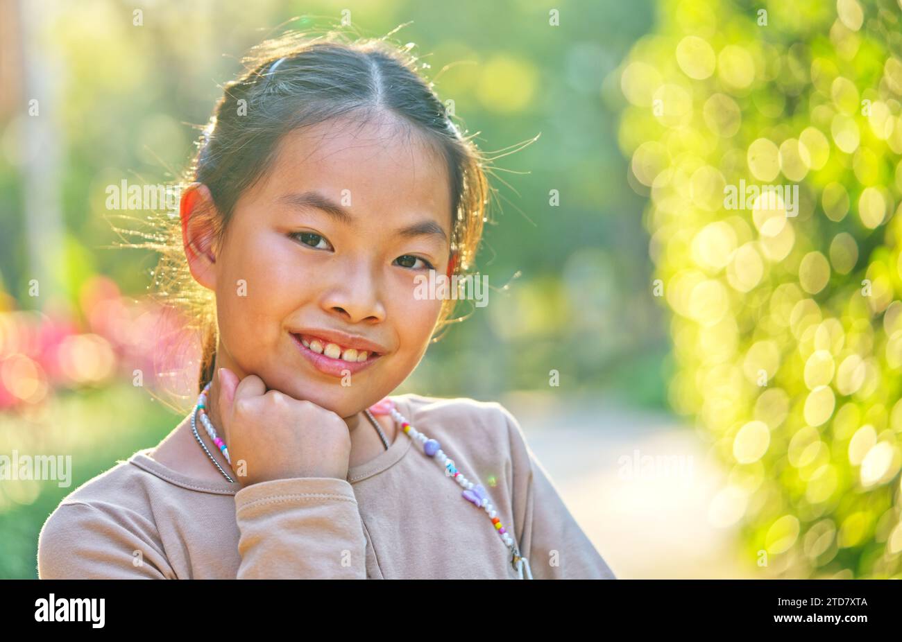 Porträt Asiatisches Mädchen im Alter von 9 oder 10 Jahren im Garten, Nahaufnahme Porträt, lächelndes Gesicht, Blick auf die Kamera, natürliches Sonnenlicht von hinten, Stockfoto
