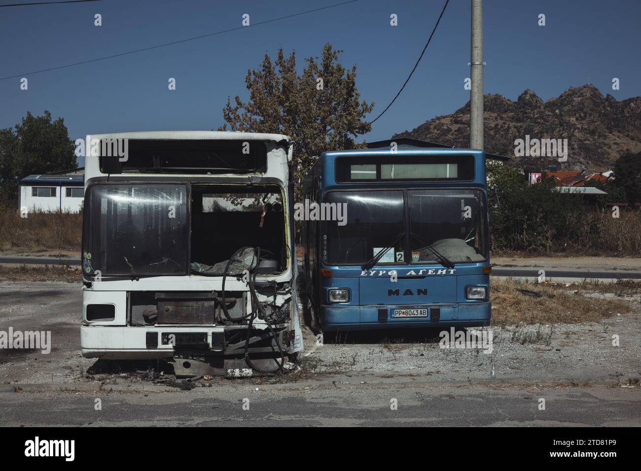 Verlassene und kaputte Busse am Stadtrand von Prilep in Nordmakedonien. Die Busse sind eindeutig unbrauchbar. Berge und blauer Himmel im Hintergrund. Stockfoto