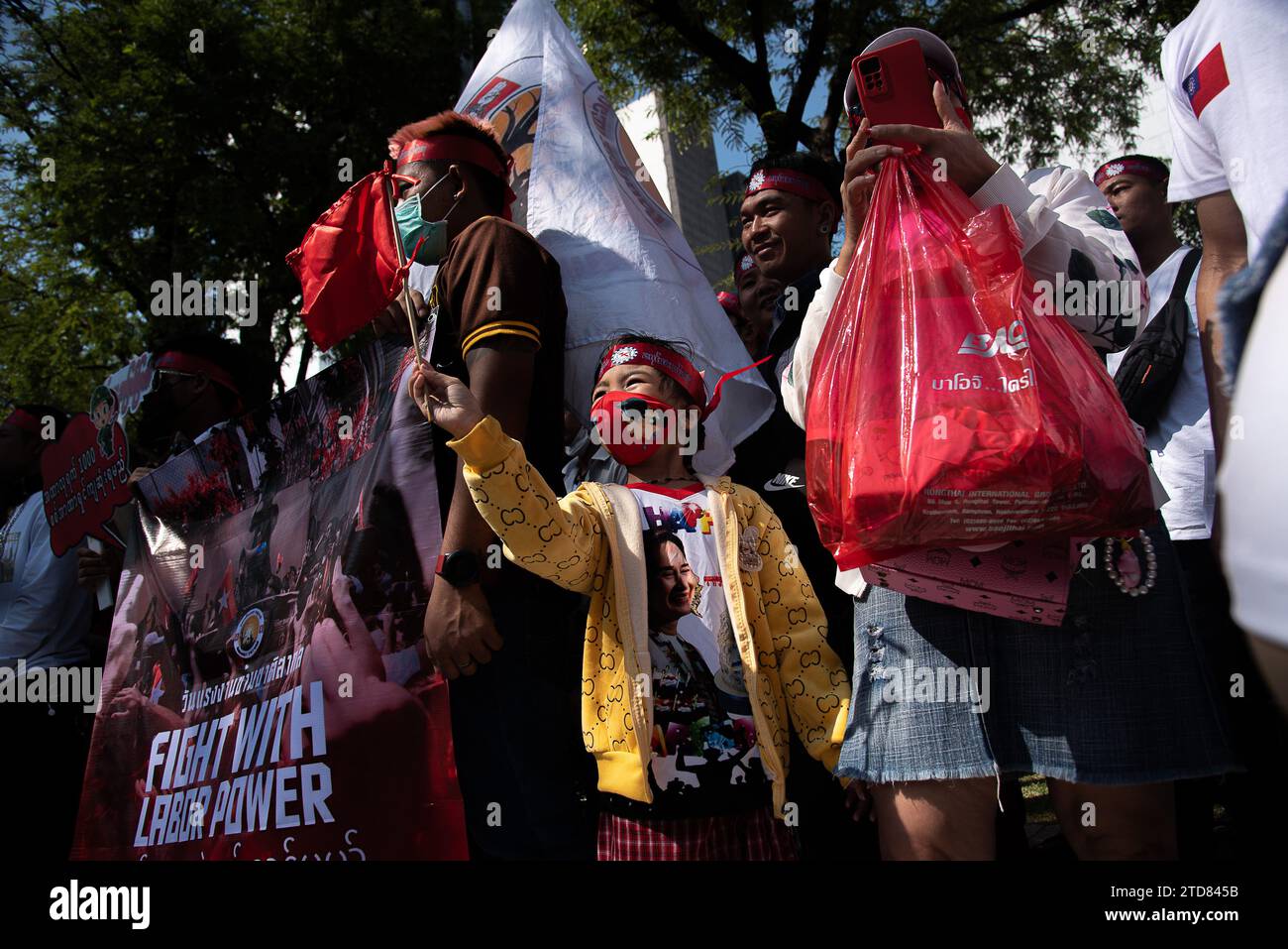 Bangkok, Thailand. Dezember 2023. Während der Demonstration vor dem Gebäude der Vereinten Nationen in Bangkok winkt ein Kind mit einer Flagge. Birmanische Arbeiter in Thailand versammelten sich vor dem Gebäude der Vereinten Nationen, um den Tag der internationalen Migranten zu feiern und gegen die Entscheidung der Militärregierung in Myanmar zu protestieren, zusätzliche zwei Prozent als Lohnsteuer von ihren im Ausland arbeitenden Bürgern zu erheben. Quelle: SOPA Images Limited/Alamy Live News Stockfoto