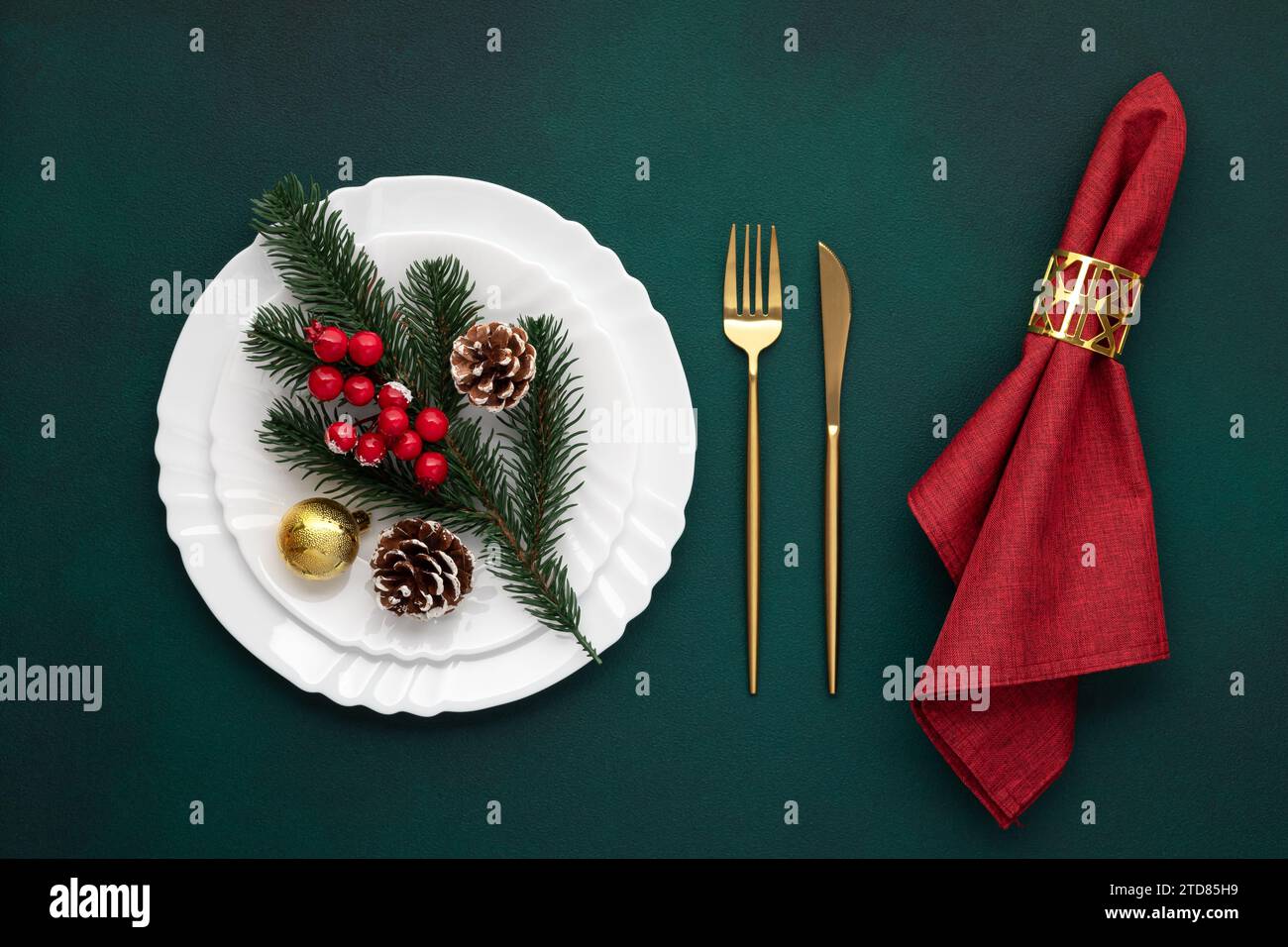 Weihnachtstisch. Weiße Platte, goldene Gabel, Messer. Tannenzweig und rote Serviette auf grünem Hintergrund. Einladungsdesign. Silvesterdekoration Stockfoto