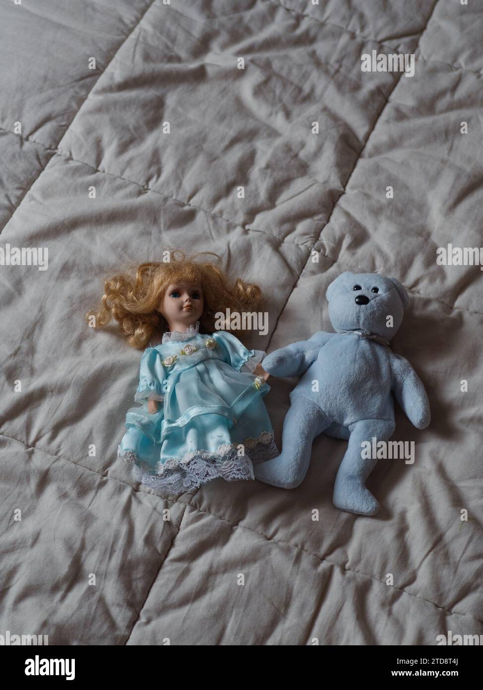 Senkrecht gerade von oben, Nahaufnahme eines blauen Teddybären und einer Lockenhaarpuppe in einem blauen Kleid auf dem Bett. Stockfoto