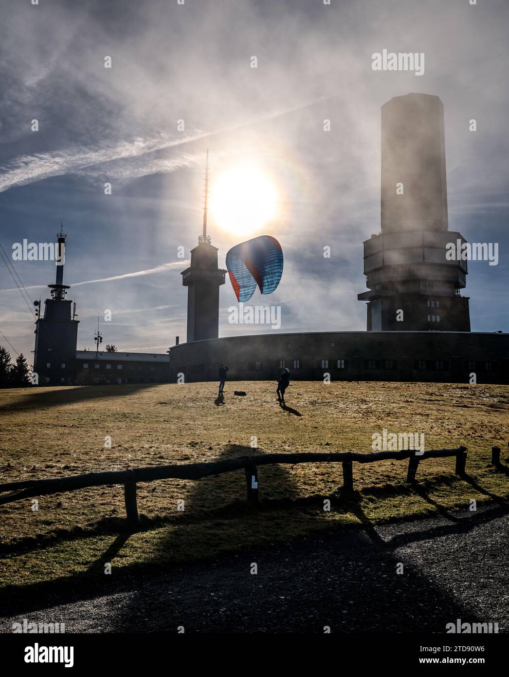 Schmitten, Deutschland. Januar 2022. Ein Mann probiert seinen Gleitschirmflieger auf dem Gipfelplateau des Großen Feldbergs im Taunus aus, während die Sonne durch dünne Wolken vom blauen Himmel scheint. Unterdessen sank die unterliegende Mainebene unter einer dicken Wolkendecke in Dunst. Frank Rumpenhorst/dpa/Alamy Live News Stockfoto Schmitten, Deutschland. Januar 2022. Ein Mann probiert seinen Gleitschirmflieger auf dem Gipfelplateau des Großen Feldbergs im Taunus aus, während die Sonne durch dünne Wolken vom blauen Himmel scheint. Unterdessen sank die unterliegende Mainebene unter einer dicken Wolkendecke in Dunst. Frank Rumpenhorst/dpa/Alamy Live News Stockfoto