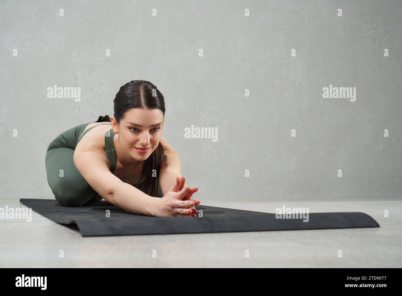 Flexible dunkelhaarige Frau, die auf Yogamatte dehnt Stockfoto