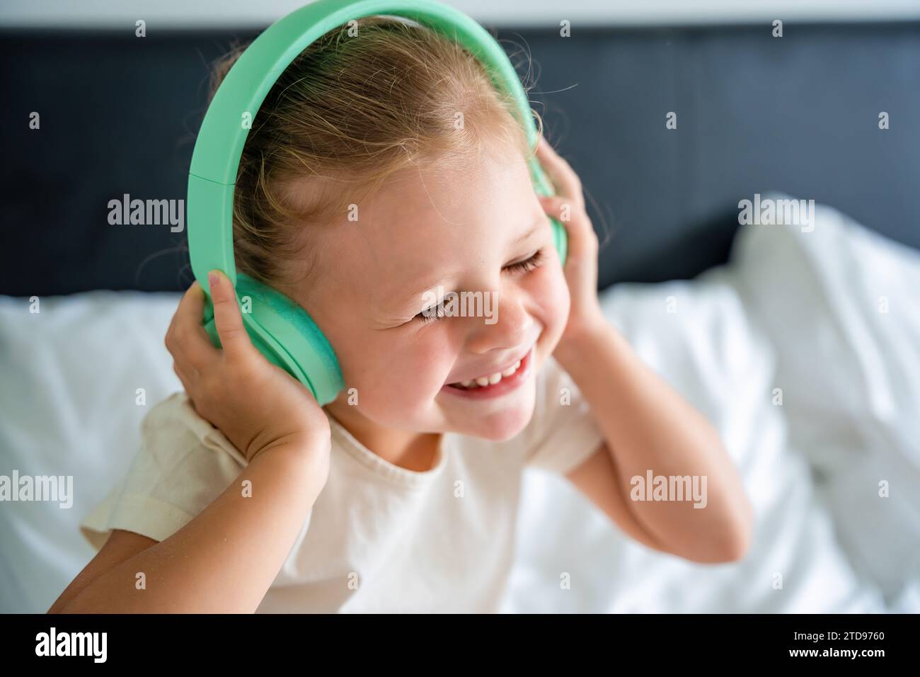 Süßes kleines Mädchen, das Musik mit grünen Kinderkopfhörern genießt Stockfoto