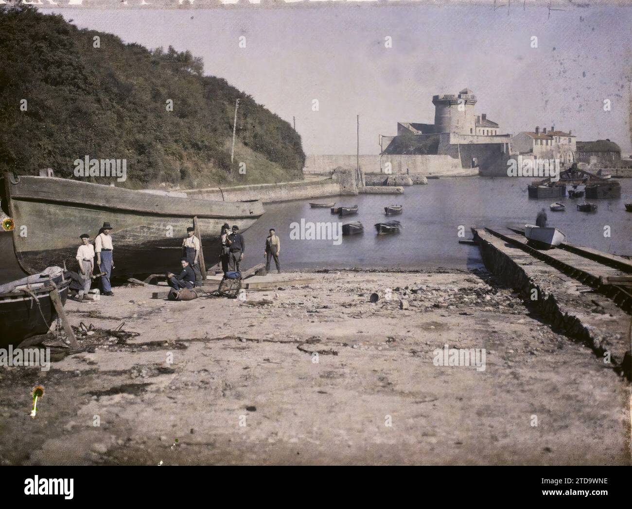 Socoa, Frankreich, Alltag, Haus, Architektur, Transport, Mensch, Meer, Ozean, Arbeitsumgebung, Turm, Bauingenieurwesen, Boot, Hafen, Befestigte Architektur, Festung, Seeverkehr, Man, Frankreich, Socoa, Pier and the fort Group of Workers Repair a Boat, Socoa, 07/10/1924 - 07/10/1924, Léon, Auguste, Fotograf, 1924 - Aquitaine - Auguste Léon, Autochrome, Foto, Glas, Autochrome, Foto, positiv Stockfoto