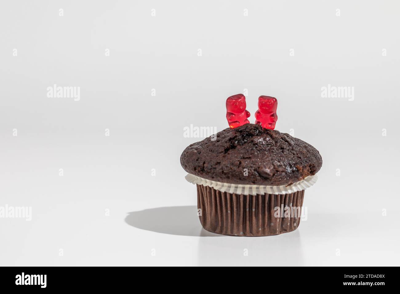 Zwei rote Gummibären auf Schokoladenmuffin auf weißem Hintergrund Stockfoto