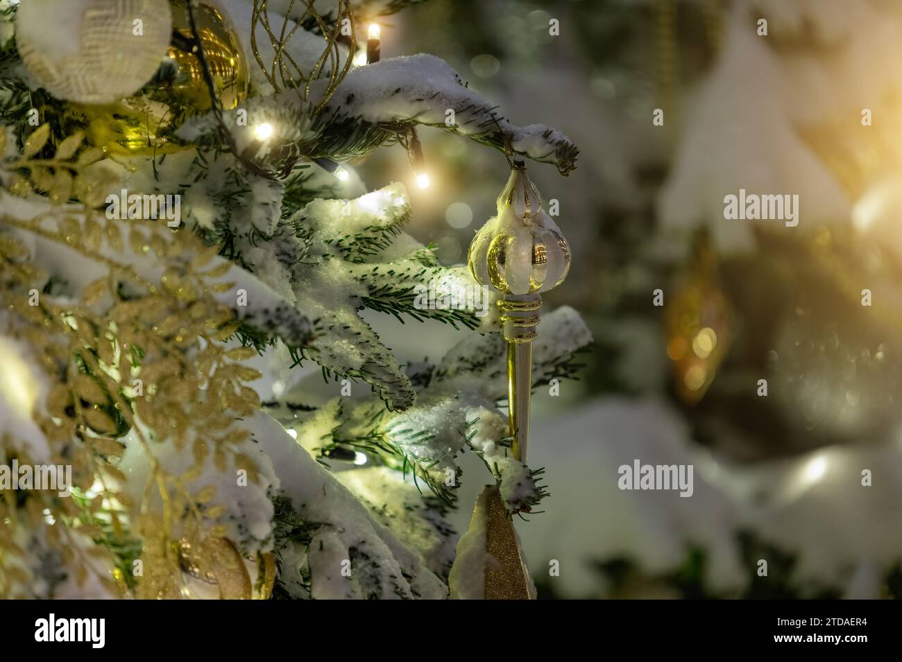 Schneebedeckter Weihnachtsbaum im Freien mit Glaskugeln und Girlanden-Lichtern. Selektiver Fokus Stockfoto