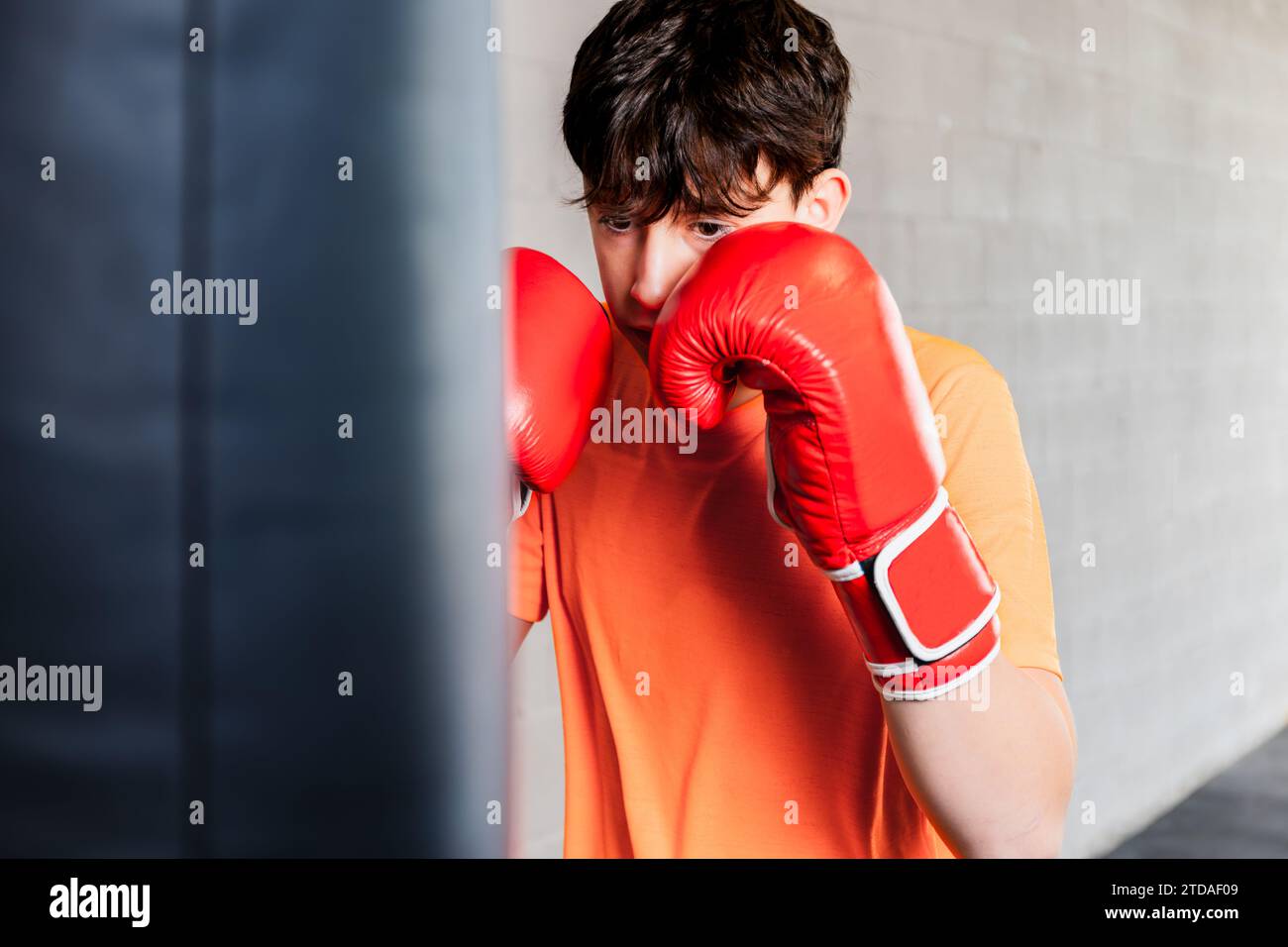 Horizontales Foto kaukasischer Teenager mit orangem T-Shirt und roten Boxhandschuhen, in einem Boxstudio. Kopierbereich. Concept Sport, Freizeit. Stockfoto