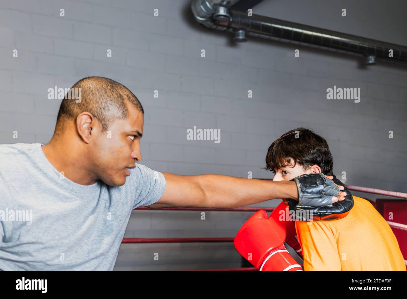 Horizontaler Foto-Junge Teenager mit orangem T-Shirt und roten Boxhandschuhen, mit seinem schwarzen Boxtrainer im Ring. Kopierbereich. Conce Stockfoto