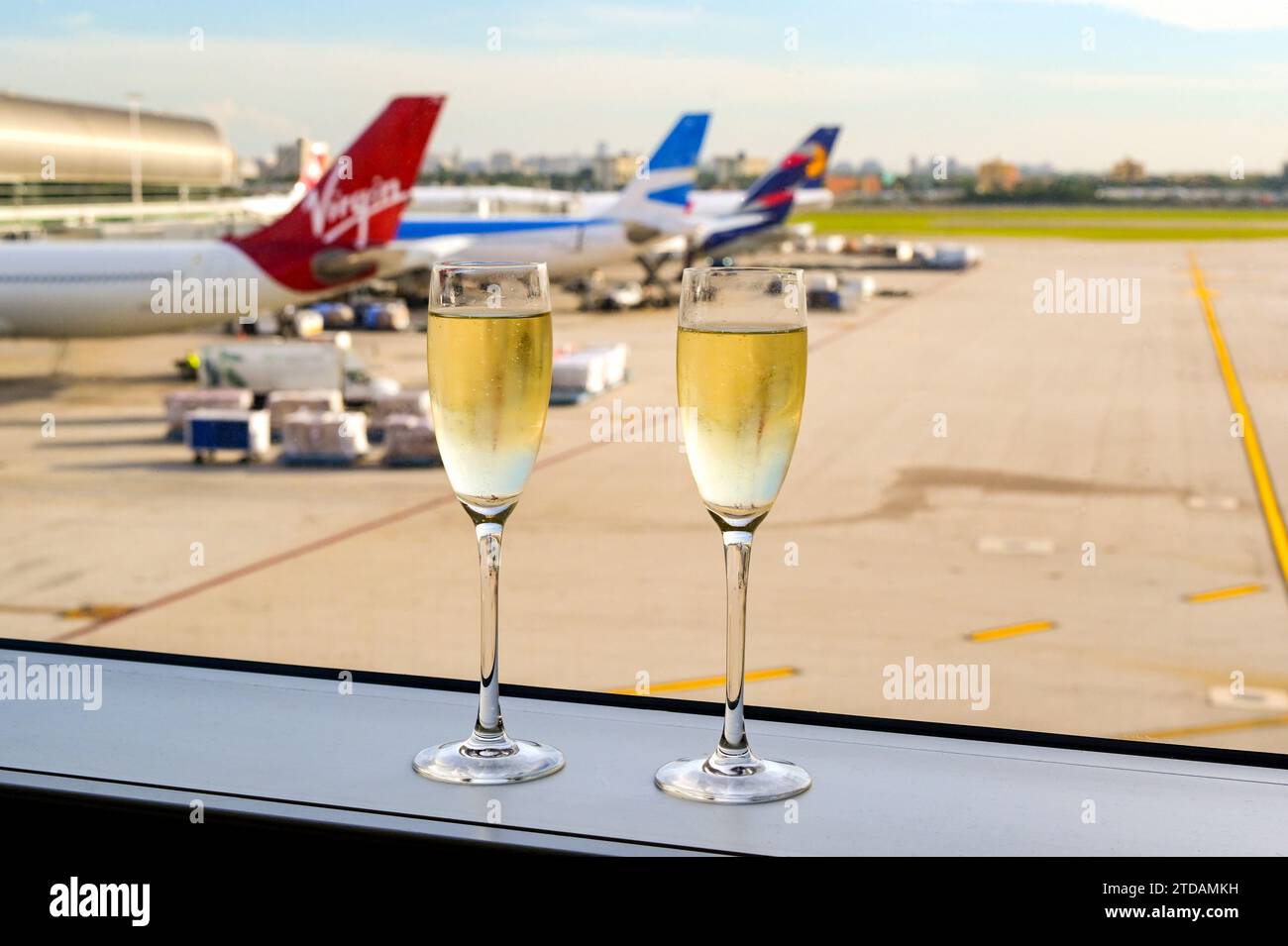 Miami, Florida, USA - 5. Dezember 2023: Zwei Gläser gekühlter Sekt auf dem Fenstervorsprung einer Flughafenlounge mit Flugzeugen im Hintergrund Stockfoto