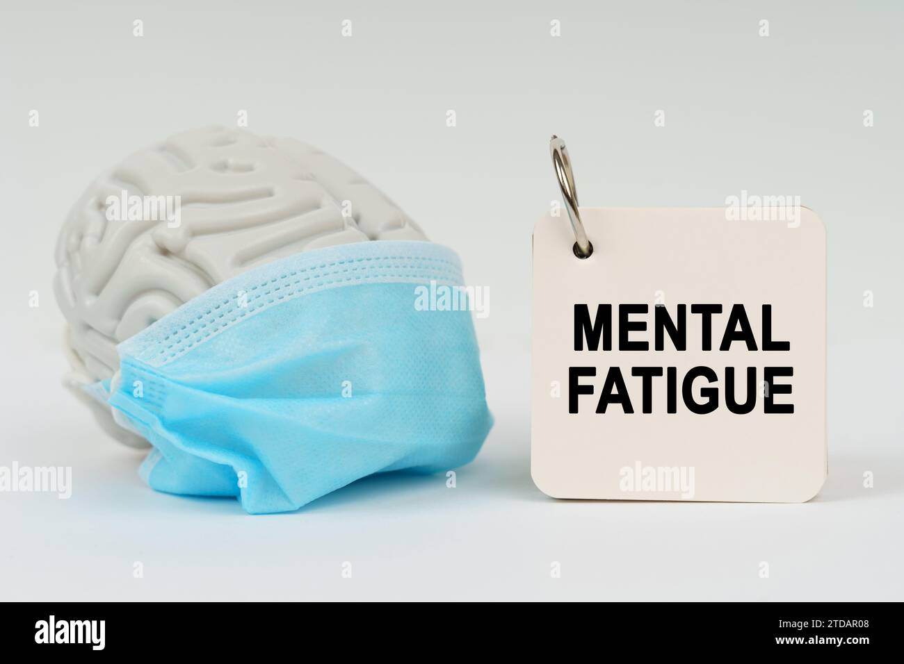 Medizinisches Konzept. Auf einer weißen Oberfläche befindet sich ein Gehirn mit einer blauen Maske und ein Notizblock mit der Inschrift "geistige Ermüdung" Stockfoto