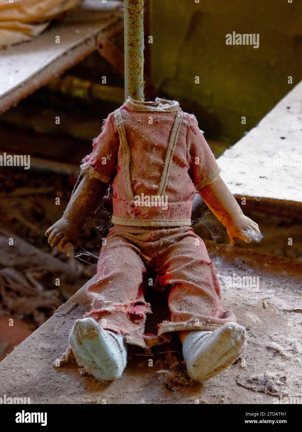 Eine Puppe mit gestreckten Armen und zerrissener Kleidung in einem verlassenen Gebäude. Kinderpuppe ohne Kopf. Ein dreckiges, kaputtes Kinderspielzeug von einem Radiati Stockfoto