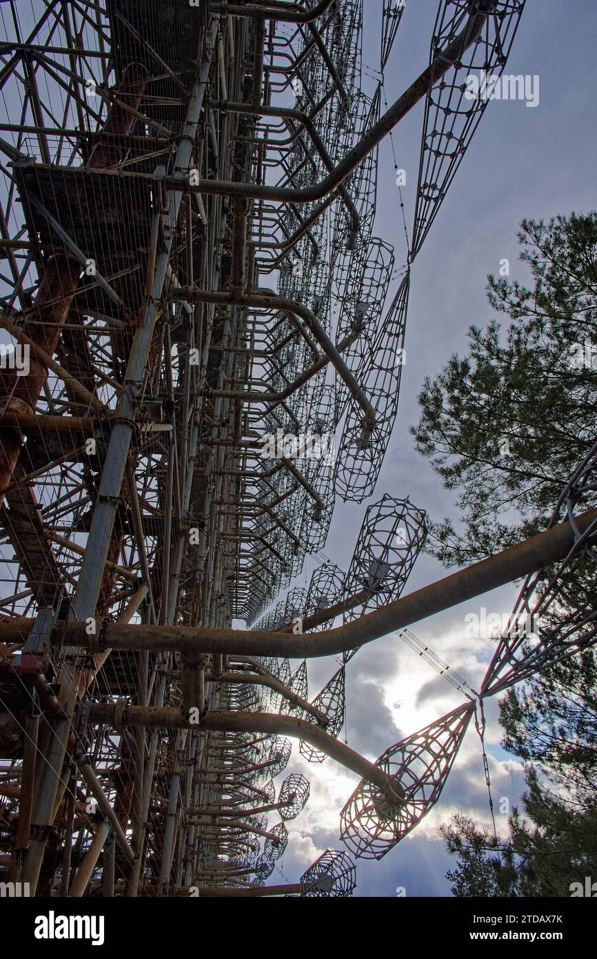 Eine komplexe Struktur aus verrosteten Metallbalken und Drahtgittern vor einem bewölkten Himmel, umgeben von Bäumen. Duga ist eine sowjetische Radarstation über dem Horizont Stockfoto