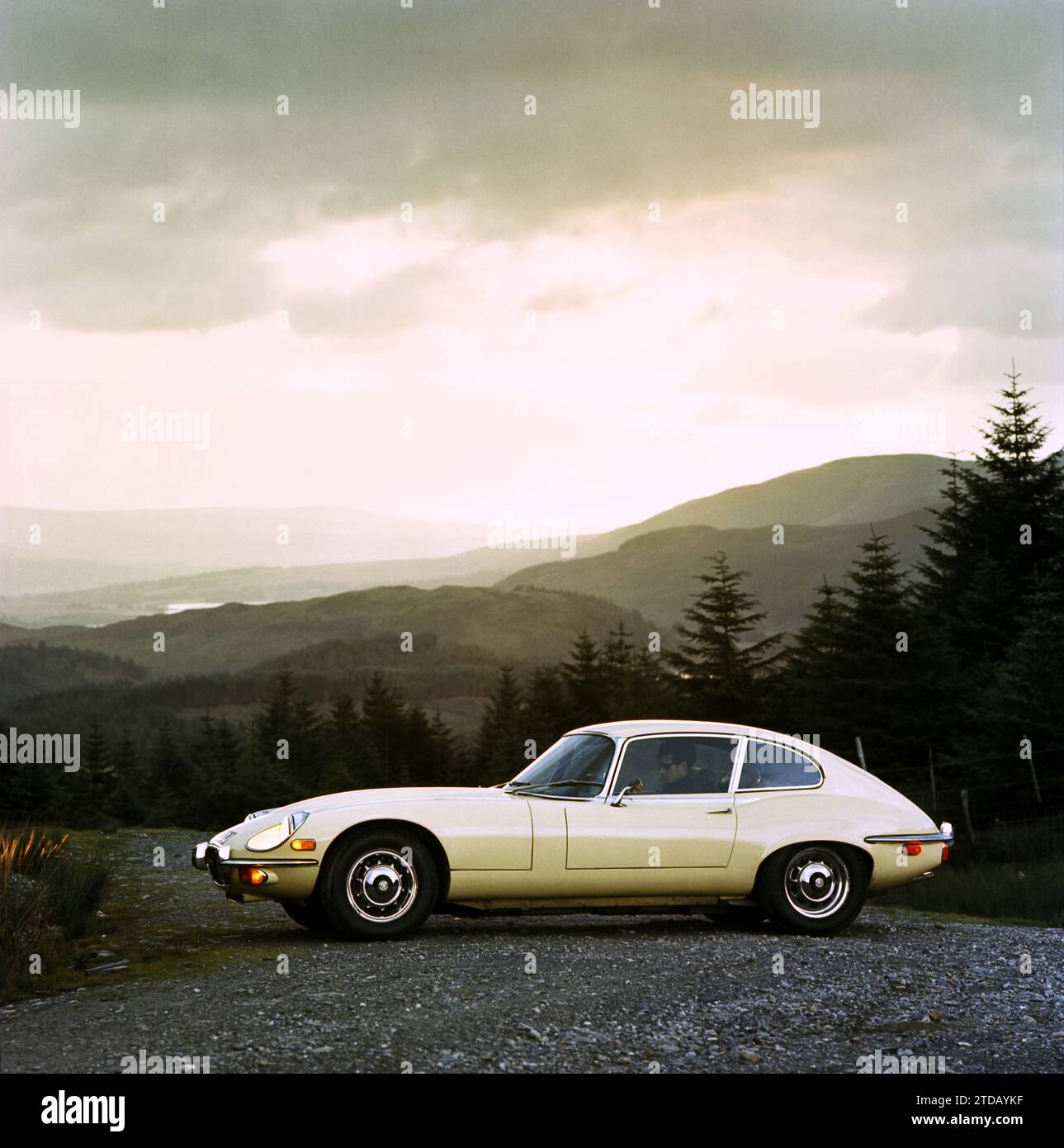 1970 Jaguar E-TYPE im Seitenprofil, Serie 3, V12, 2+2 TRW920J auf hoher Straße mit Blick auf Wälder, Berge und Seen in den schottischen Highlands Stockfoto