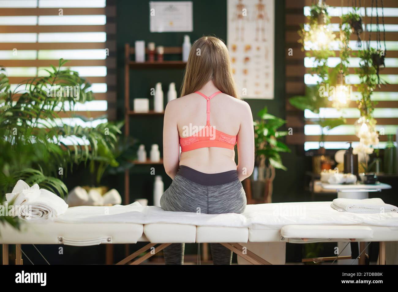 Gesundheitszeit. Von hinten gesehen Teenager Mädchen in medizinischem Massagetherapeuten Schrank auf Massagetisch sitzend. Stockfoto