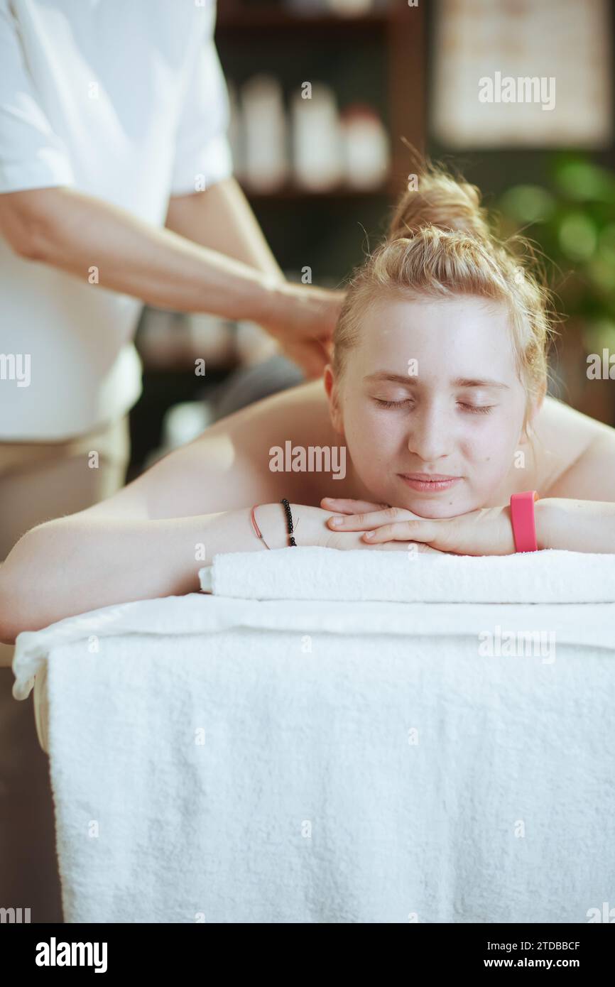 Gesundheitszeit. Massagetherapeutin Frau im Massageschrank mit Teenager-Klientin, die Massage auf dem Massagetisch macht. Stockfoto