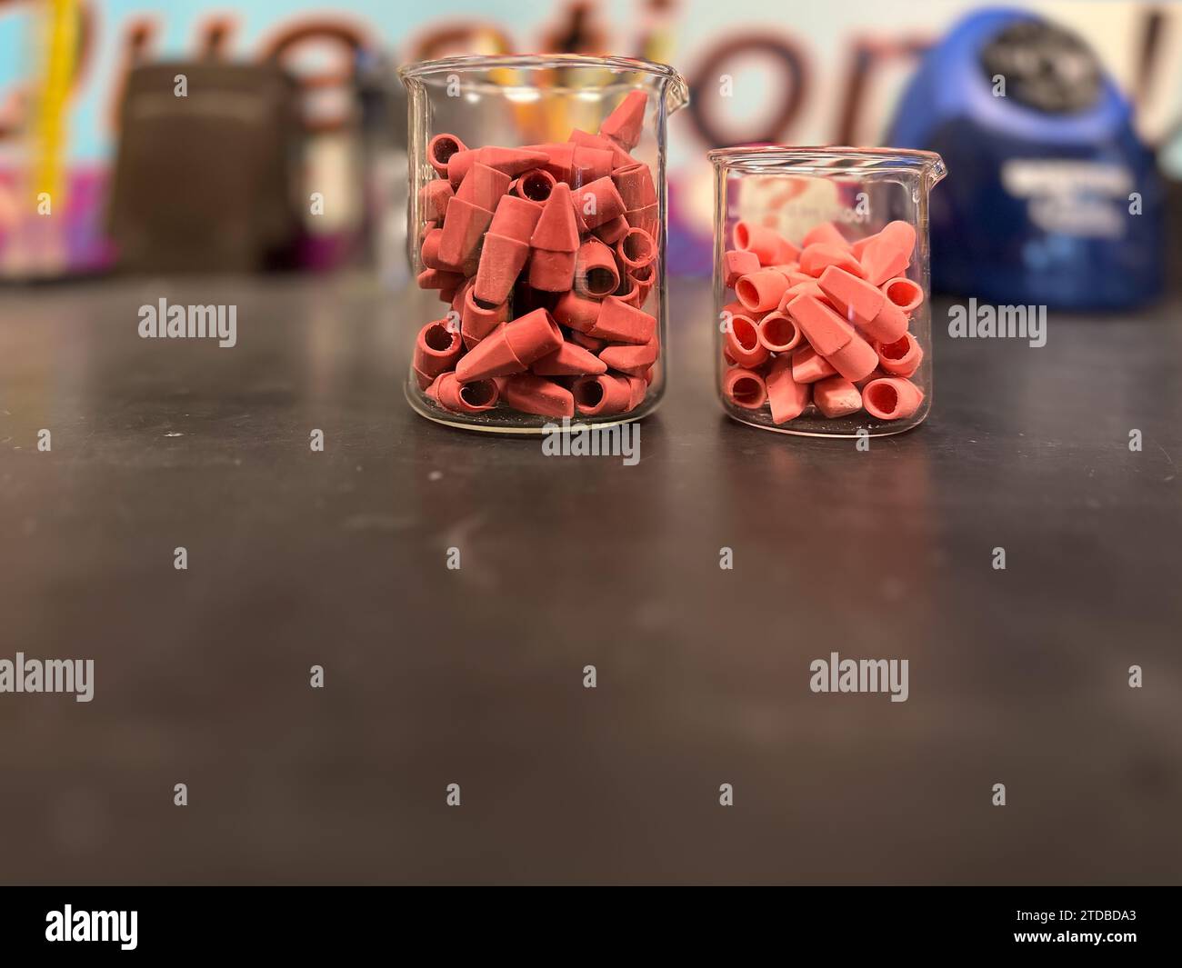 Rosafarbene Radiergummis in einem Laborbecher aus Klarglas auf einem schwarzen Tisch. Stockfoto