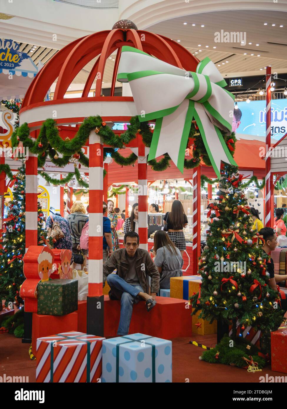 Ein Thai-Mann sitzt in einem Weihnachtskiosk in der Mall Lifestore Bangkapi. Thailand ist überwiegend buddhistisch, so dass Weihnachten kein offizieller Feiertag ist, aber das Land schafft es, den Sanuk (Genuss) dieser festlichen Zeit zu genießen und ihm eine deutlich thailändische Note zu verleihen. Hinzu kommt der offenkundige kommerzielle Aspekt, den thailändische Einzelhändler und Werbetreibende Weihnachten schnell als Marketinginstrument nutzen. Stockfoto