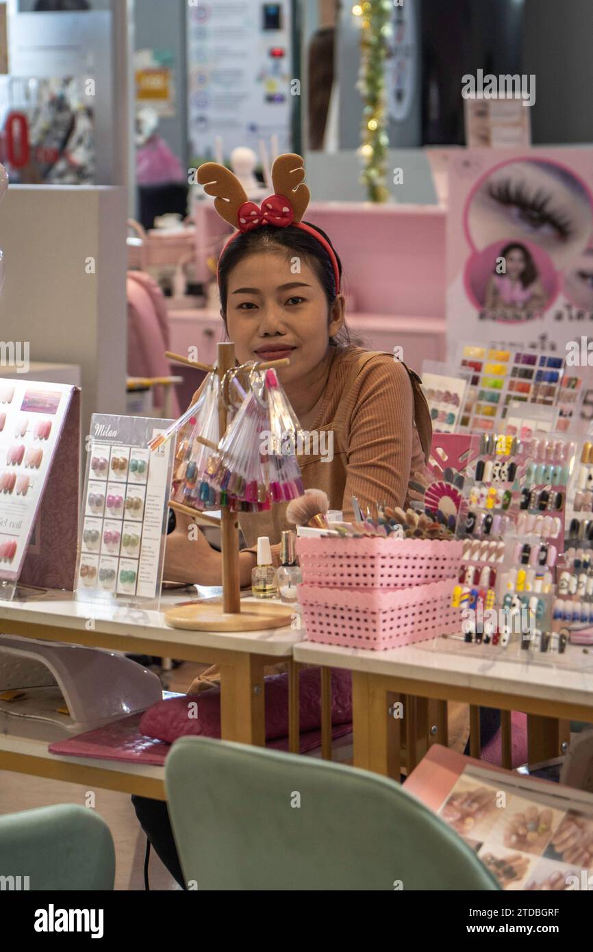 Bangkok, Thailand. Dezember 2023. An ihrem Stand im Lotus Super Center Bankapi wartet eine thailändische Manikürerin mit Weihnachtsbügel auf Kunden. Thailand ist überwiegend buddhistisch, so dass Weihnachten kein offizieller Feiertag ist, aber das Land schafft es, den Sanuk (Genuss) dieser festlichen Zeit zu genießen und ihm eine deutlich thailändische Note zu verleihen. Hinzu kommt der offenkundige kommerzielle Aspekt, den thailändische Einzelhändler und Werbetreibende Weihnachten schnell als Marketinginstrument nutzen. (Foto: Nathalie Jamois/SOPA Images/SIPA USA) Credit: SIPA USA/Alamy Live News Stockfoto